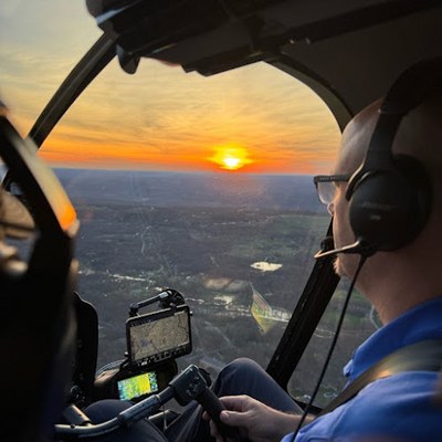Walter Dusseldorp at the controls of an R-44 helicopter at sunset